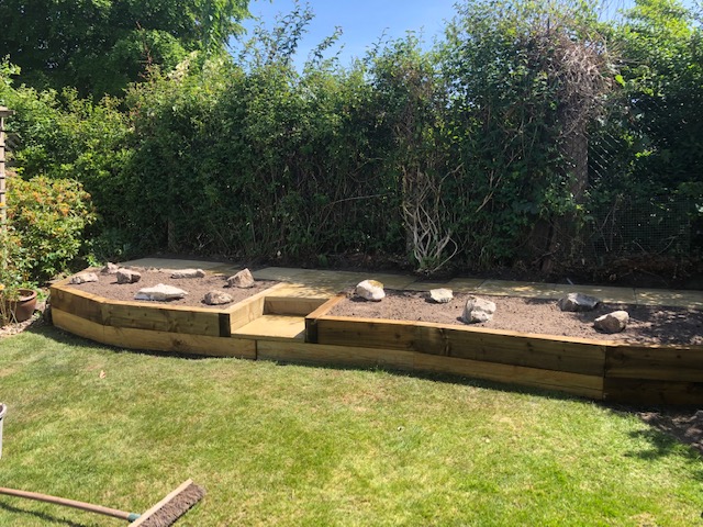 Small retaining wall out of wooden sleepers with two steps up to a pathway for working in the rockery